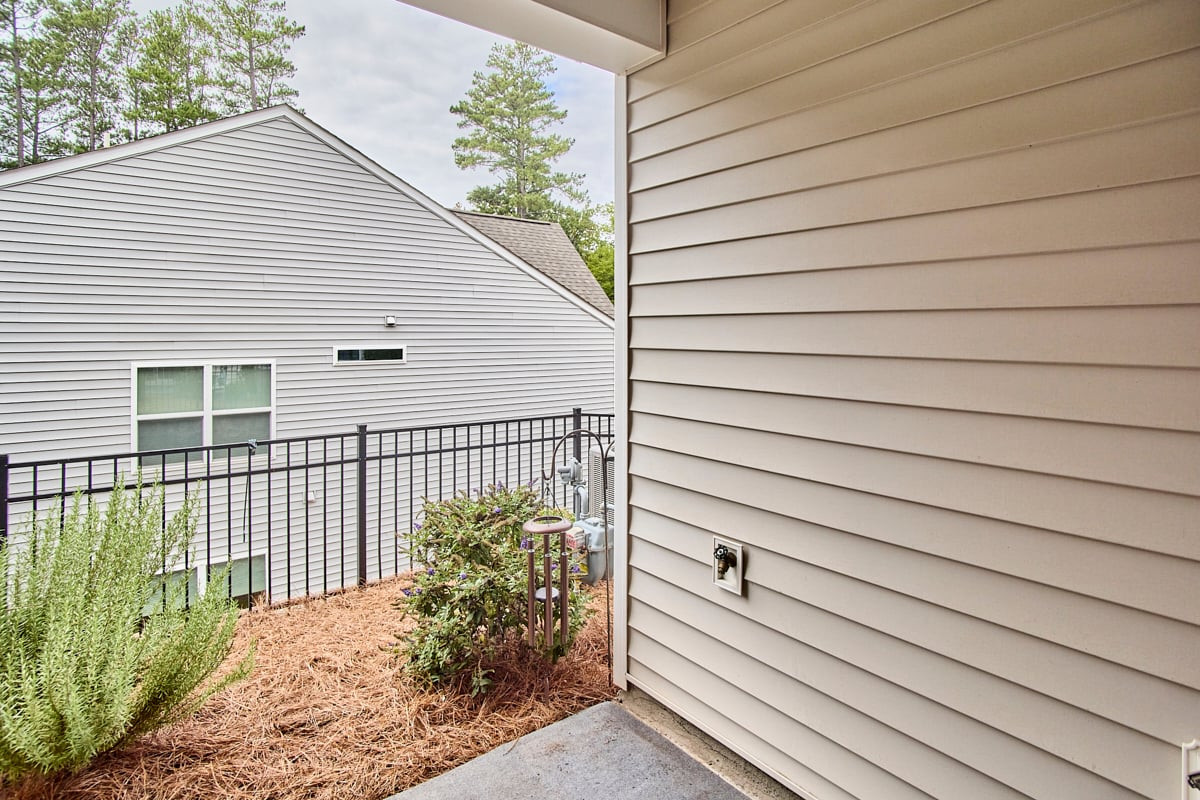 Small patio with a black railing, mulched garden beds, and a neighboring house.