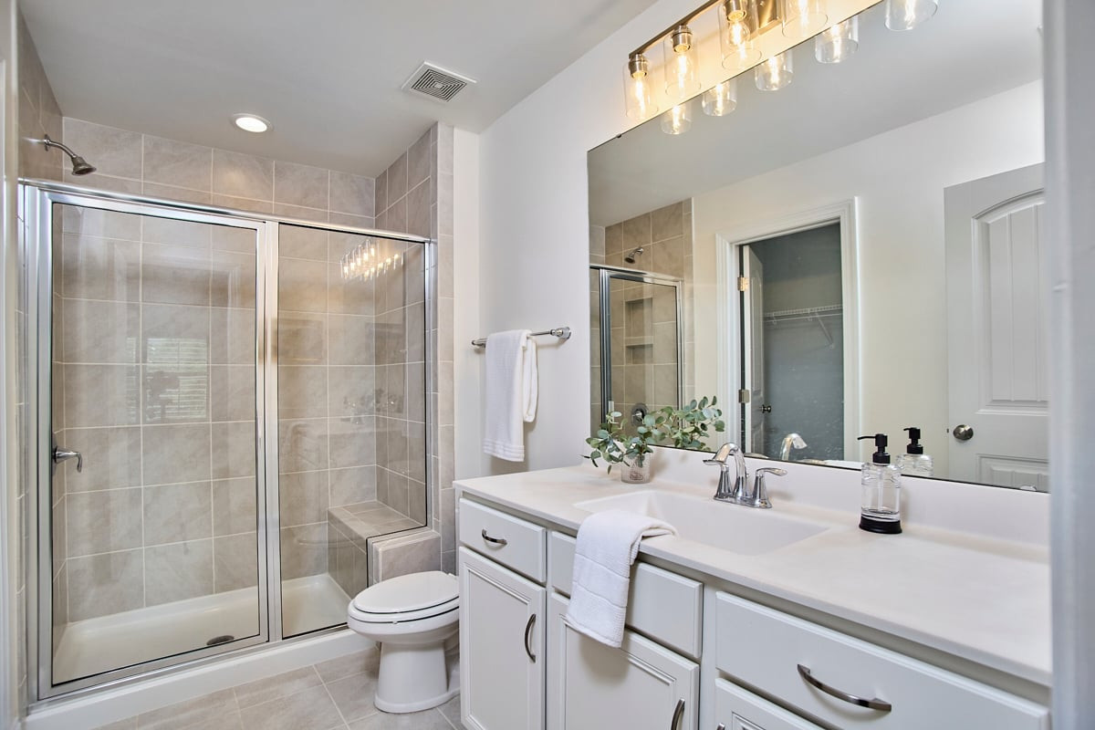 Bathroom with a tiled glass shower and long white vanity beneath a large mirror.