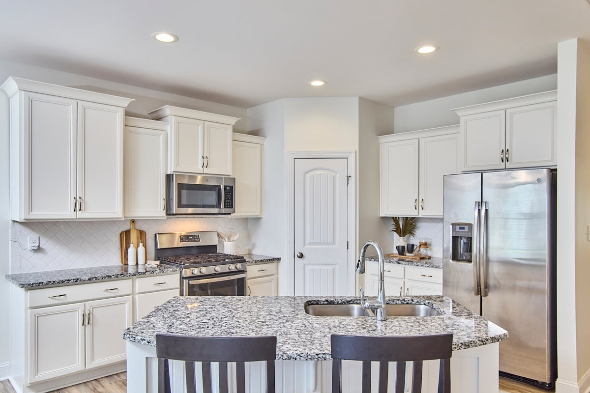 Kitchen with a granite island sink, white cabinetry, and stainless steel appliances.