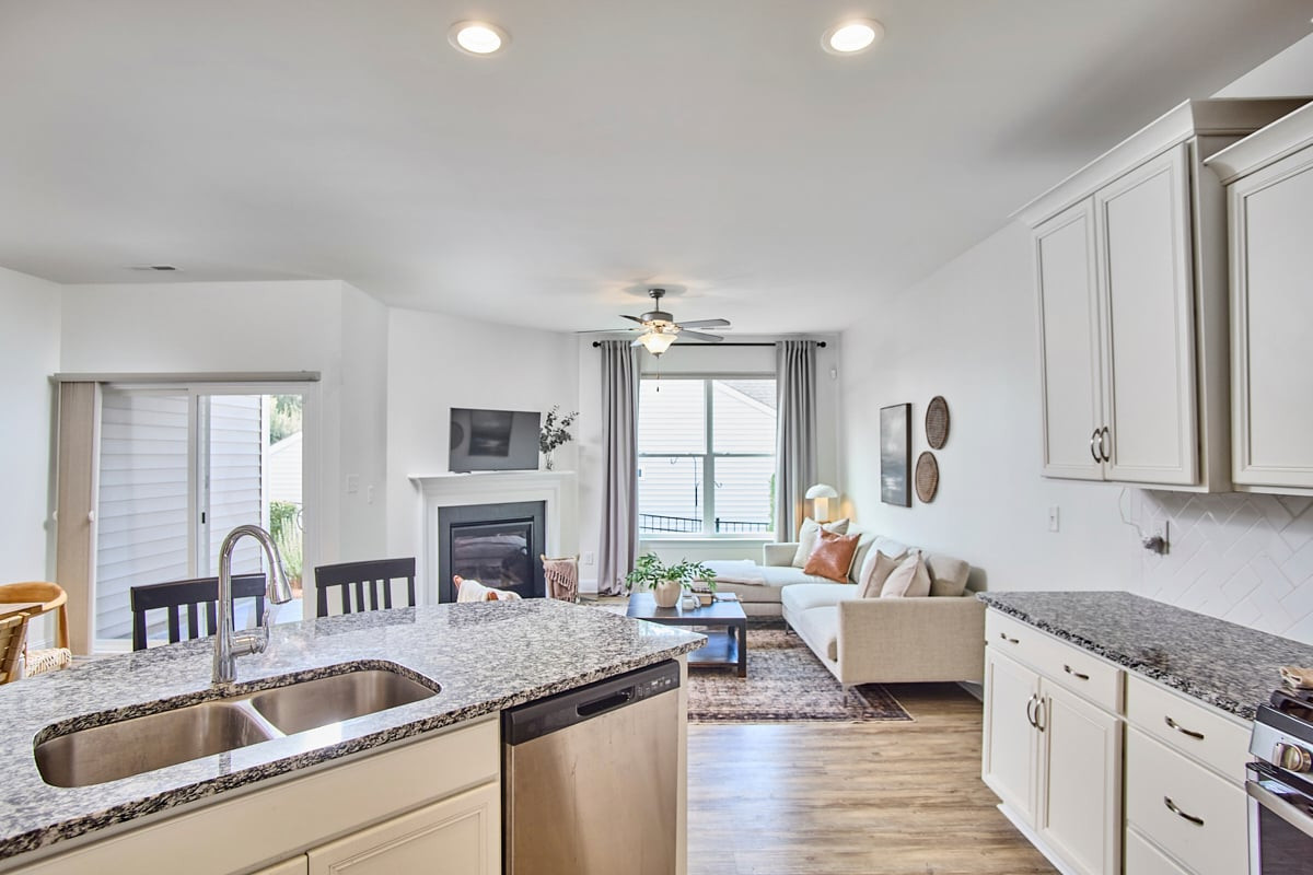 Open kitchen and living room with granite counters, white cabinets, and a fireplace.