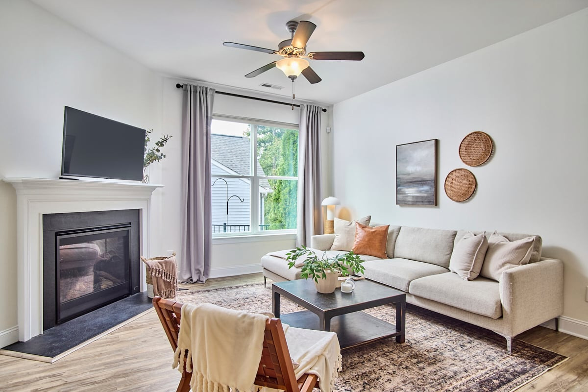Staged living room with a light sectional sofa, fireplace, and large curtained window.