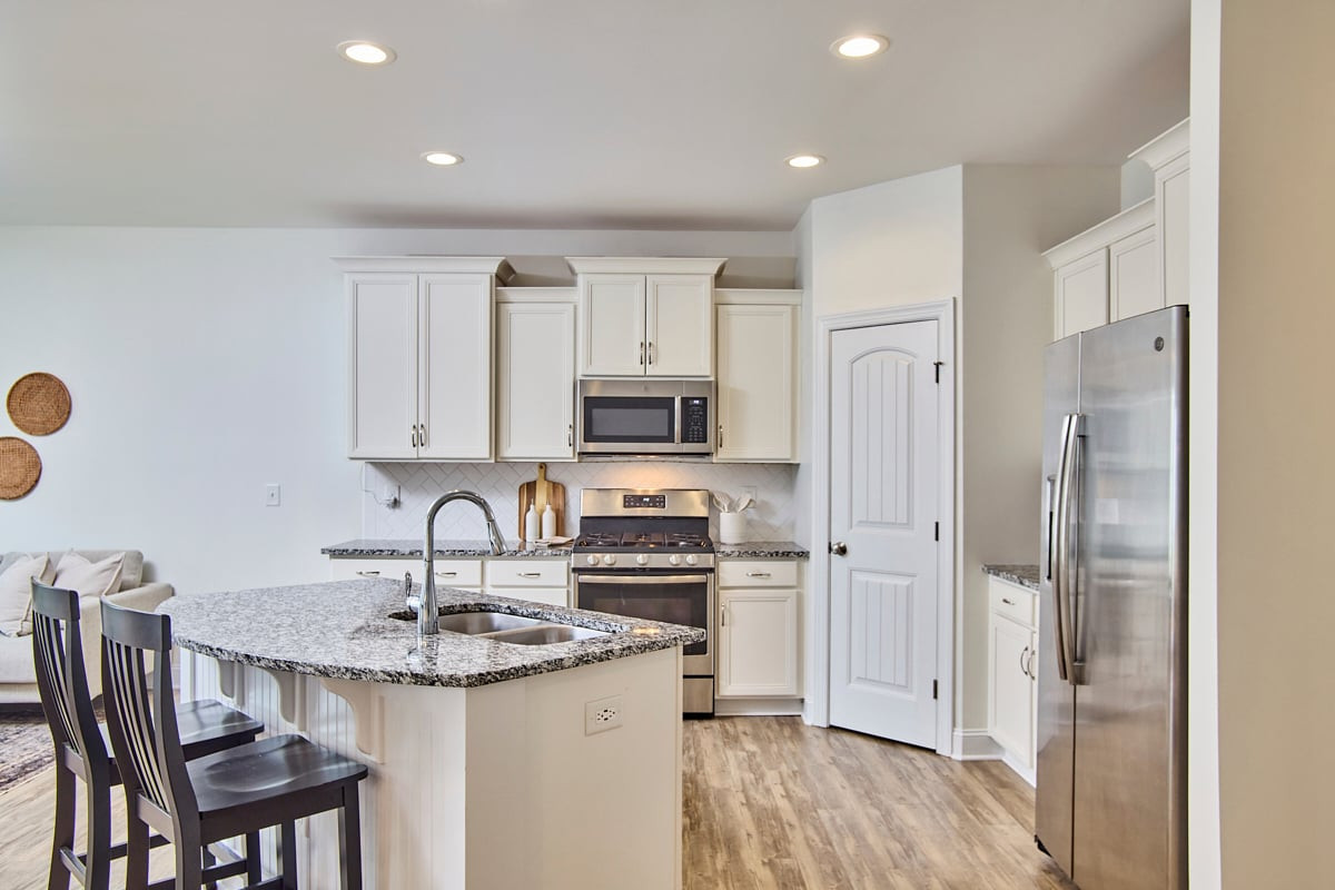 Kitchen with a granite island, white cabinets, stainless steel appliances, and wood-look floors.