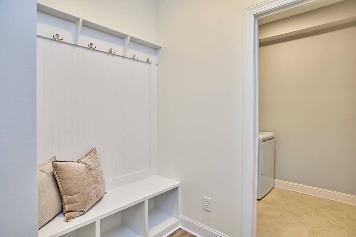 Mudroom with a built-in bench and coat hooks beside a tiled laundry area.