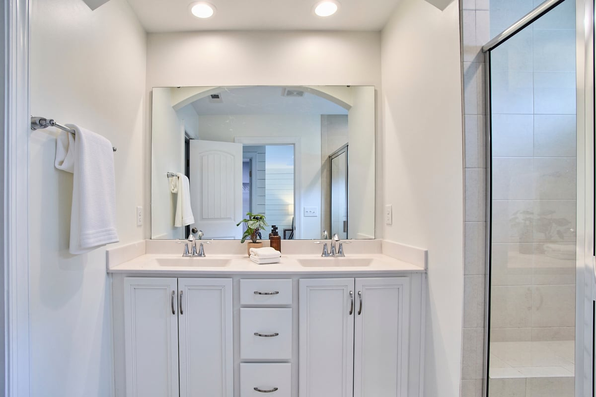 Bathroom with a white double vanity and a glass-enclosed tiled shower.