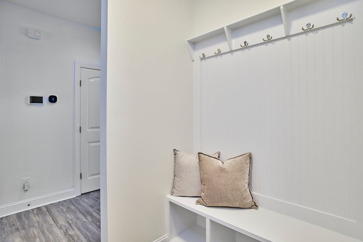Entryway with a white built-in bench, coat hooks, beige pillows and gray wood-look flooring.