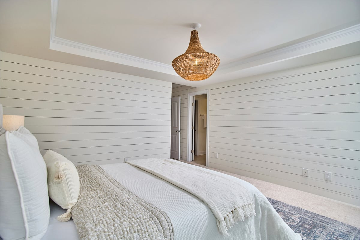 Bedroom with white shiplap walls, a layered bed, and a woven pendant light.