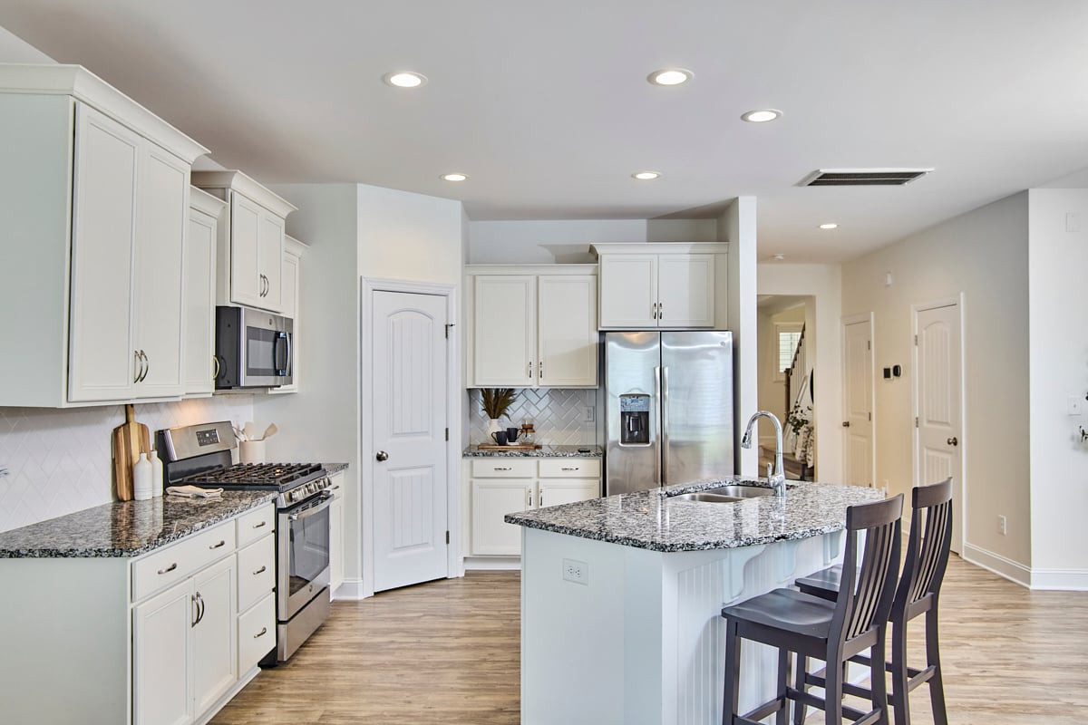 Kitchen with white cabinets, stainless steel appliances, granite counters, and a large island with bar stools.