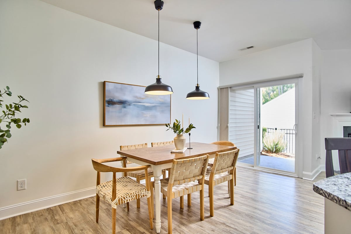 Dining room with a wooden table, woven chairs, pendant lights, and sliding glass doors.