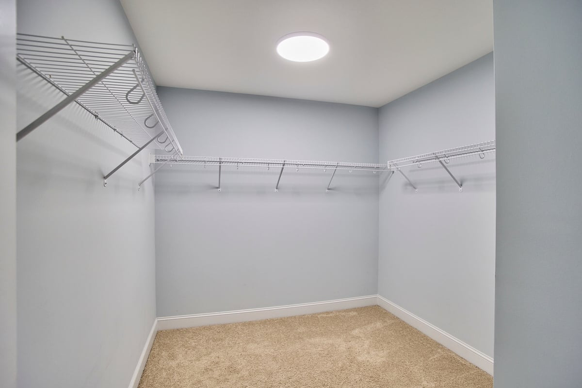 Walk-in closet with wire shelving on three walls, beige carpet, and a round ceiling light.