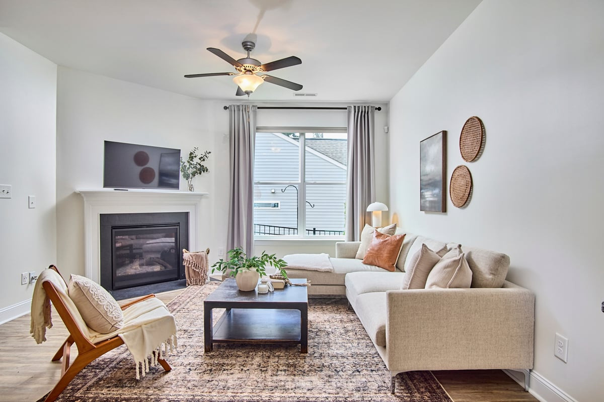 Living room with a beige sectional, fireplace, large curtained window, and ceiling fan.