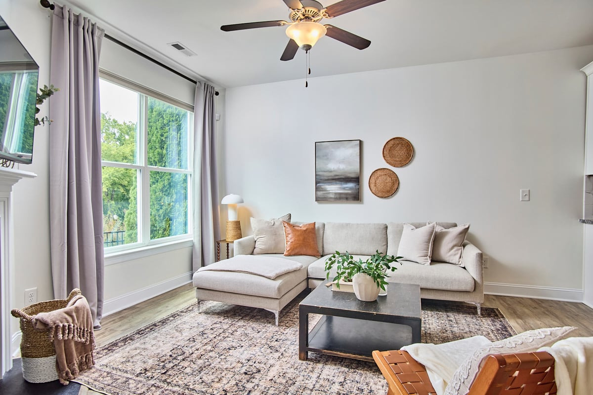 Living room with a light sectional, patterned rug, and large windows overlooking greenery.