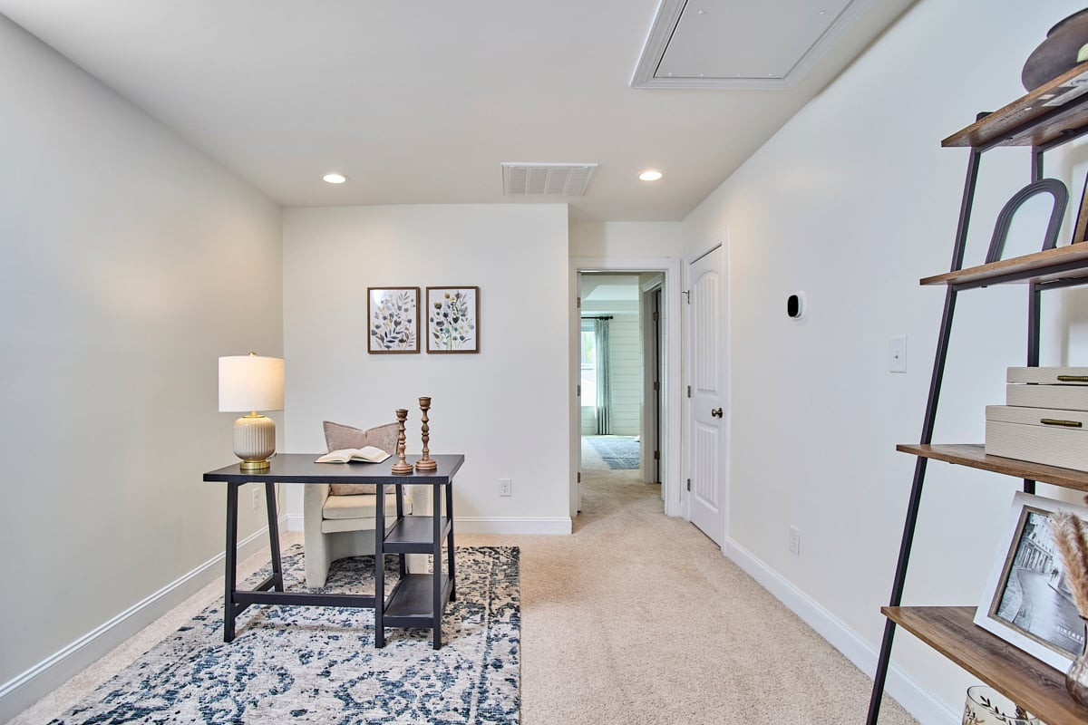 Staged home office with a black desk, armchair, patterned rug, and open shelving.