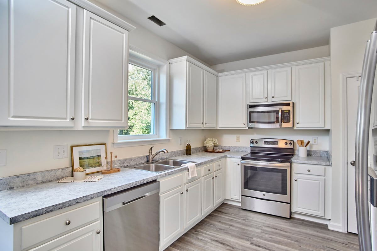 Bright kitchen with white cabinets, stone counters, stainless steel appliances, and a window over the sink.