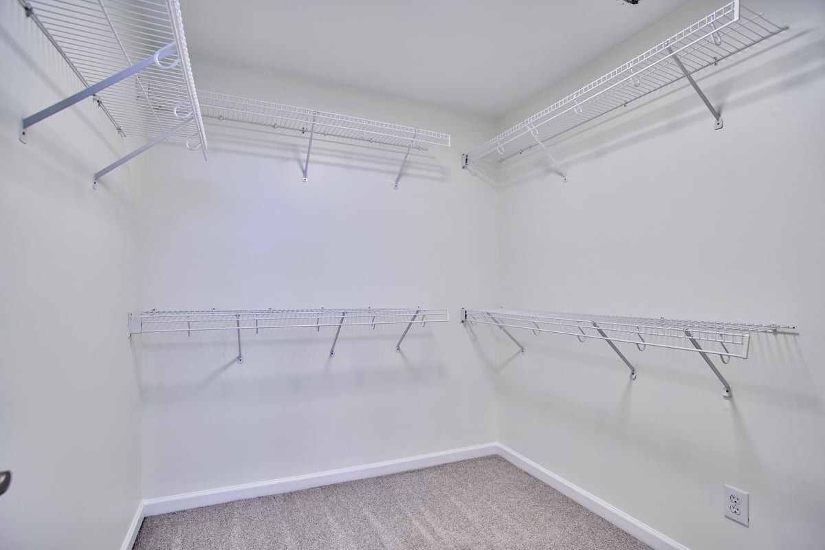 Walk-in closet with white wire shelving on three walls and carpeted floor.