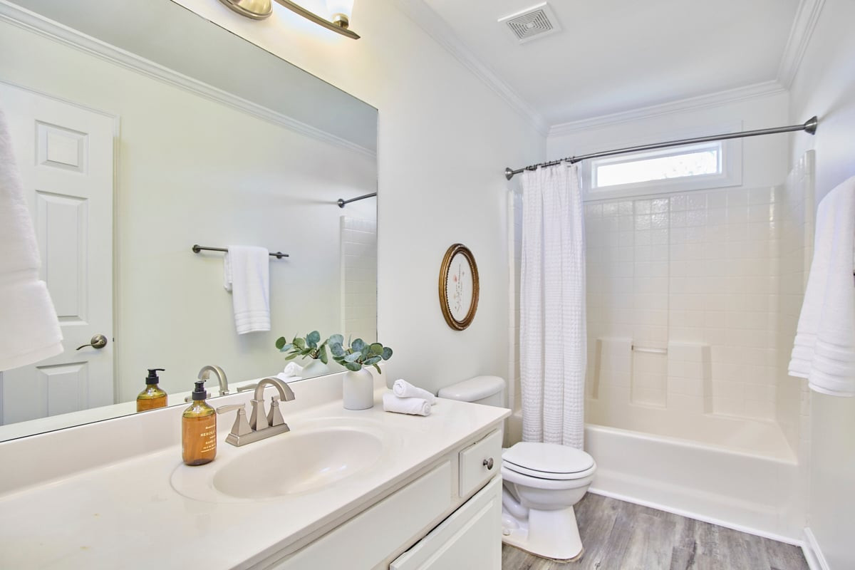 Bathroom with a white vanity, oval sink, tub-shower, and gray wood-look flooring.