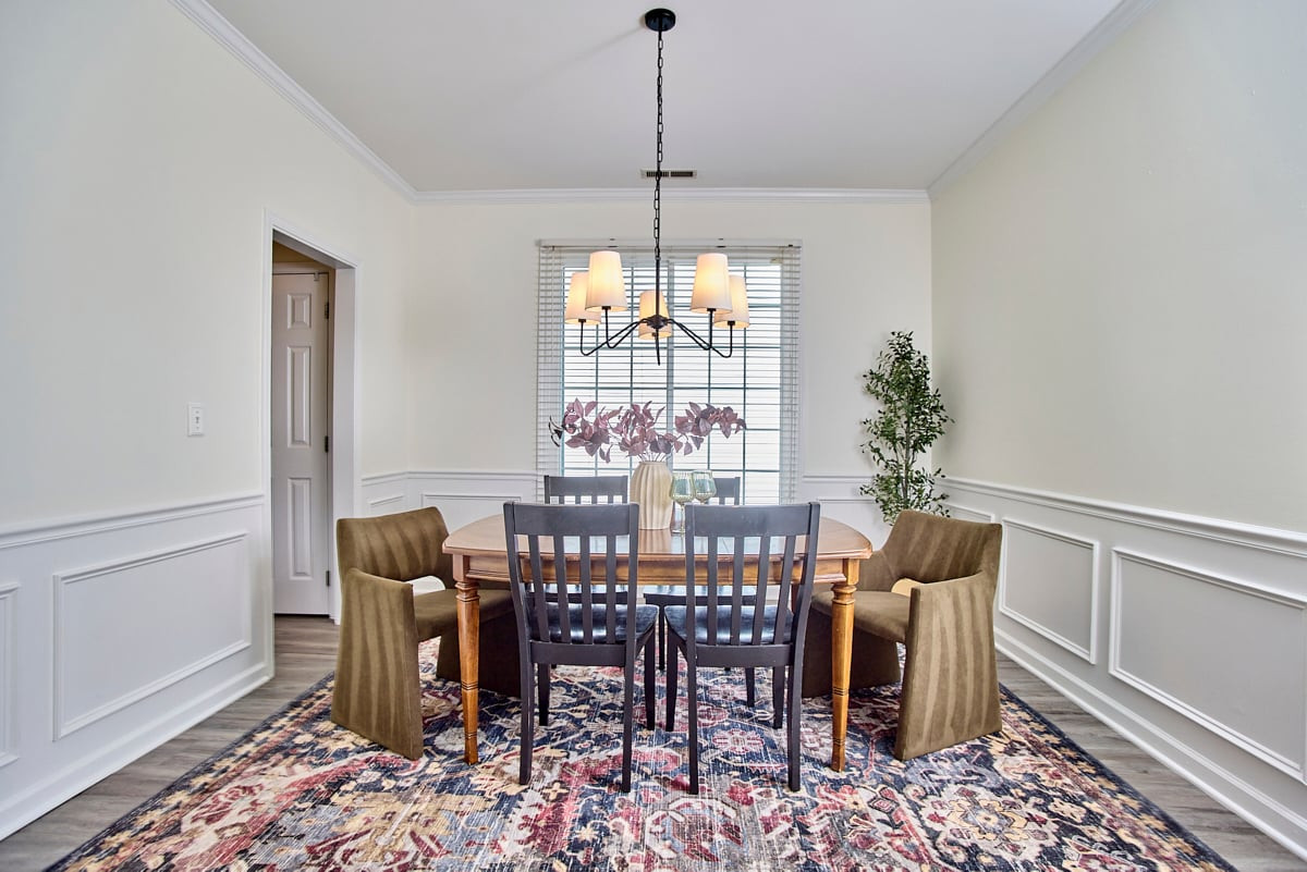 Dining room with a wood table, upholstered chairs, chandelier, and patterned rug.