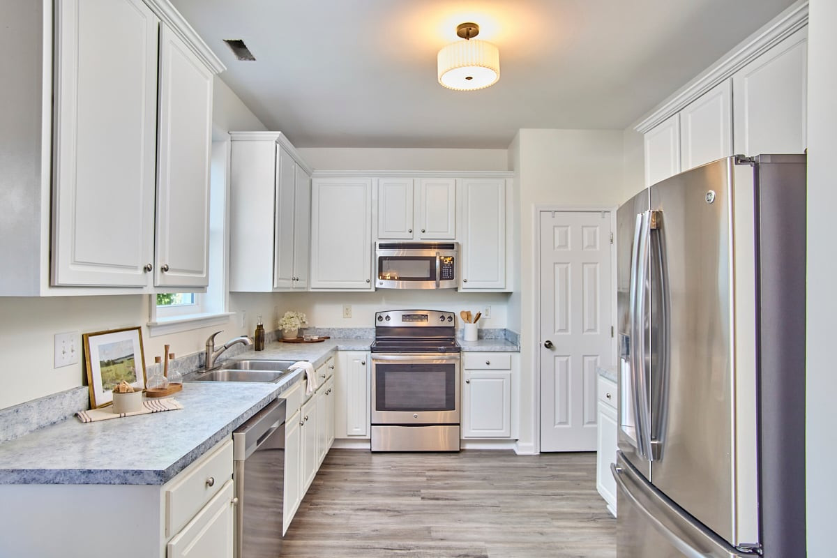 Bright white kitchen with stainless steel appliances, gray counters, and a central cooking range.