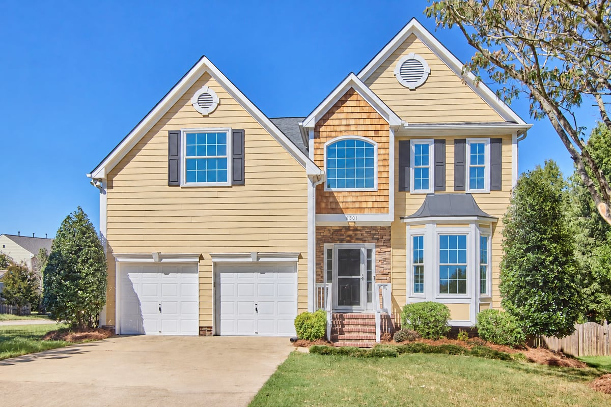 Two-story yellow house with twin garages, stone accents, and a front lawn.