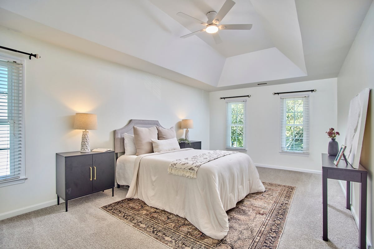 Staged bedroom with a large bed beneath a vaulted ceiling and ceiling fan.