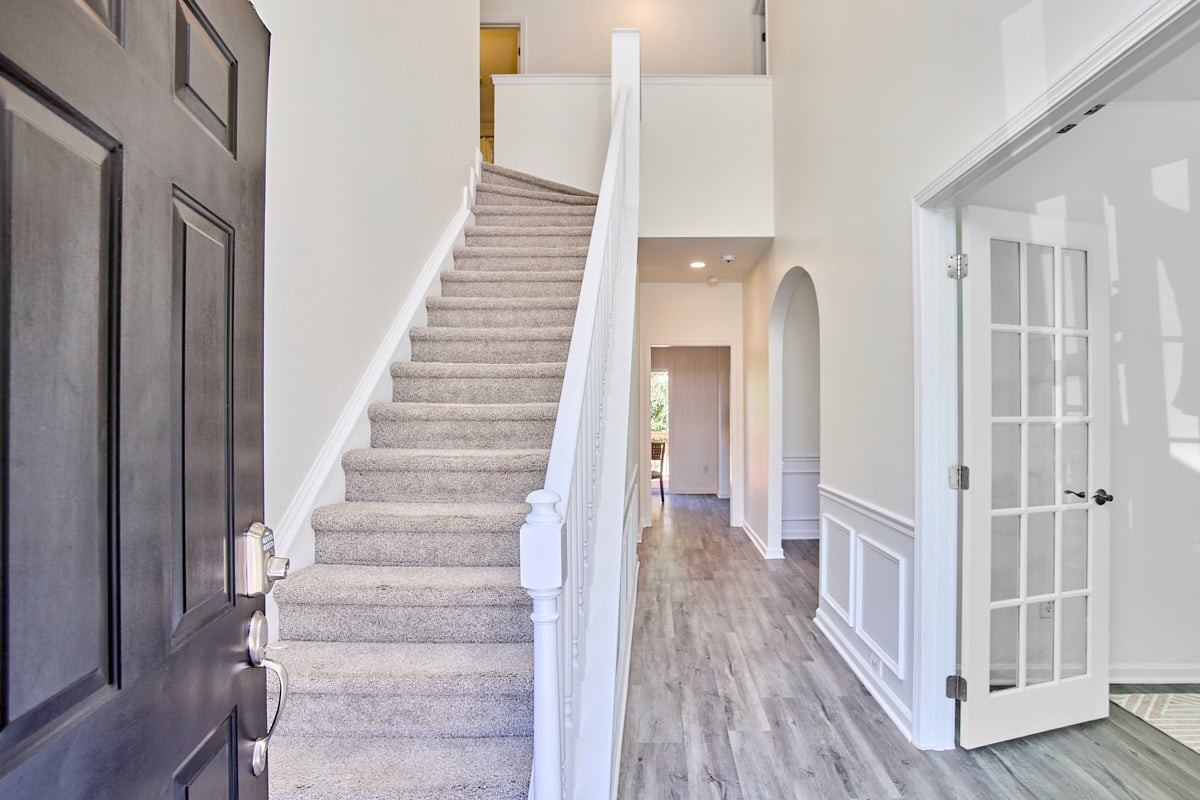 Entry foyer with carpeted staircase, dark front door, and wood-look flooring.