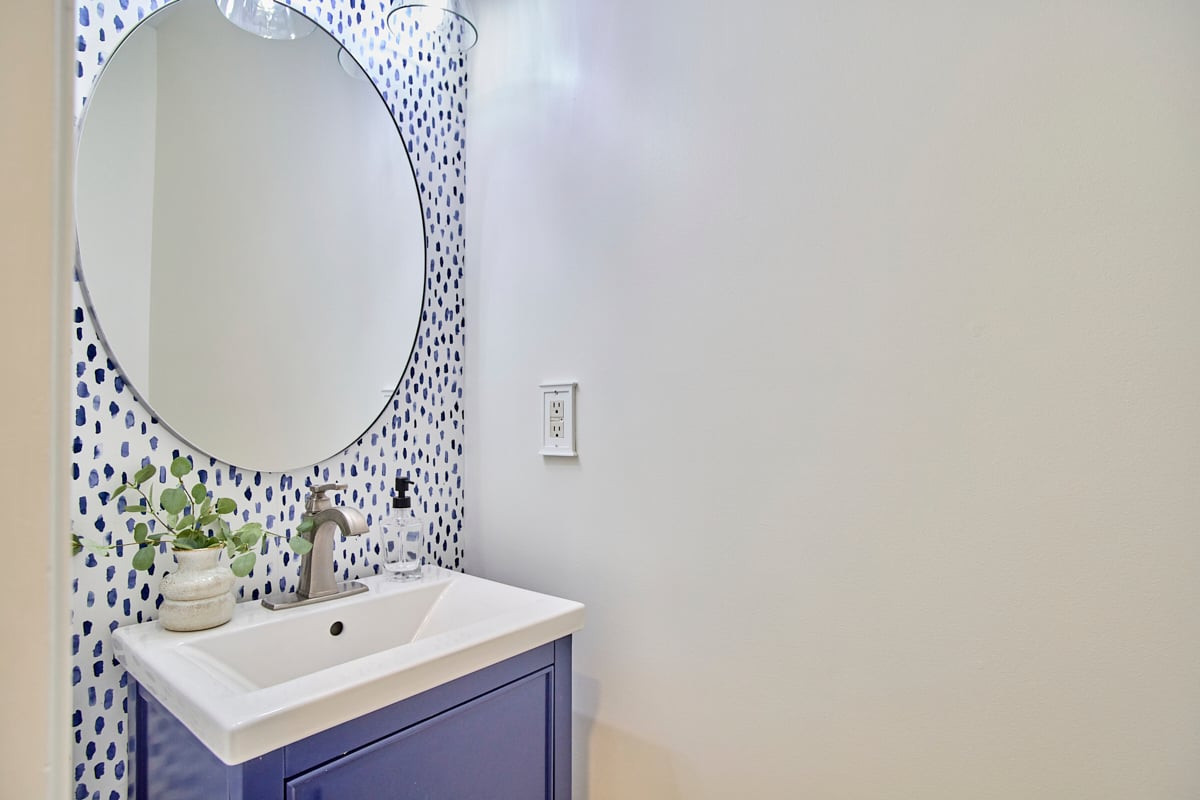 Bathroom vanity with a blue cabinet, patterned tile backsplash, and large round mirror.