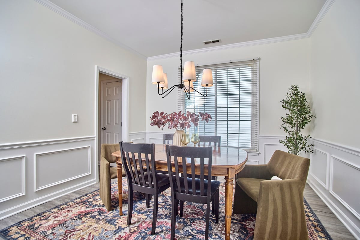 Dining room with a wood table, upholstered chairs, decorative wall paneling, and a chandelier.