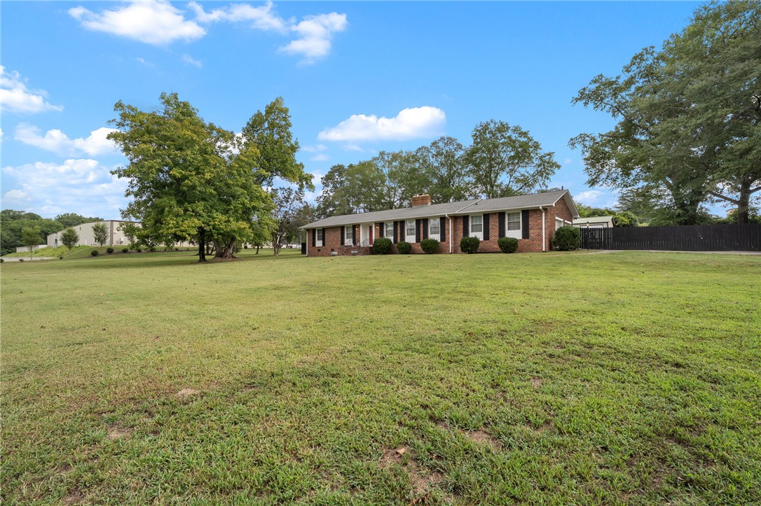 Single-story brick house with dark shutters, a broad lawn, mature trees, and a black fence.