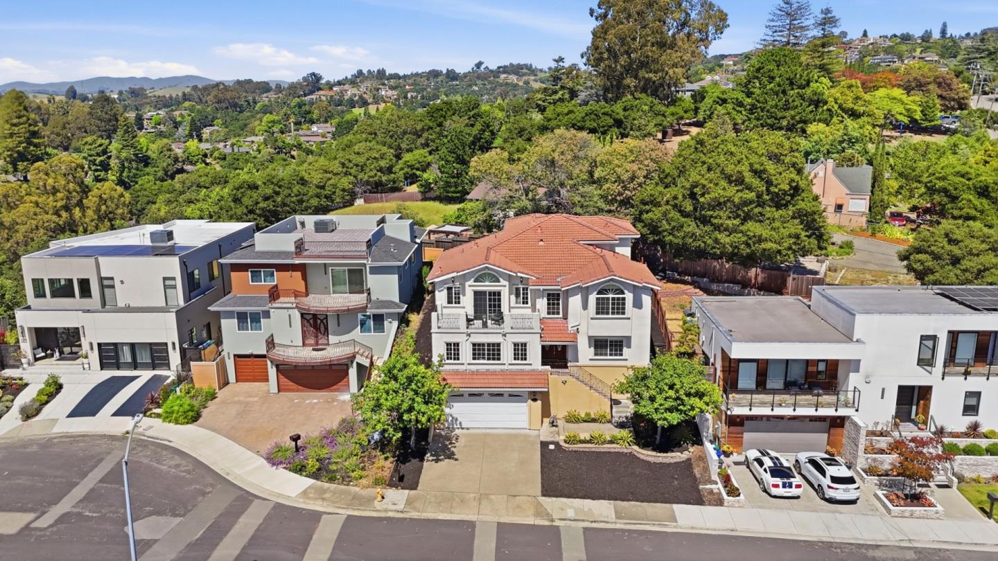 Aerial view of a two-story, red-tile-roof home amid wooded hills and neighboring houses.