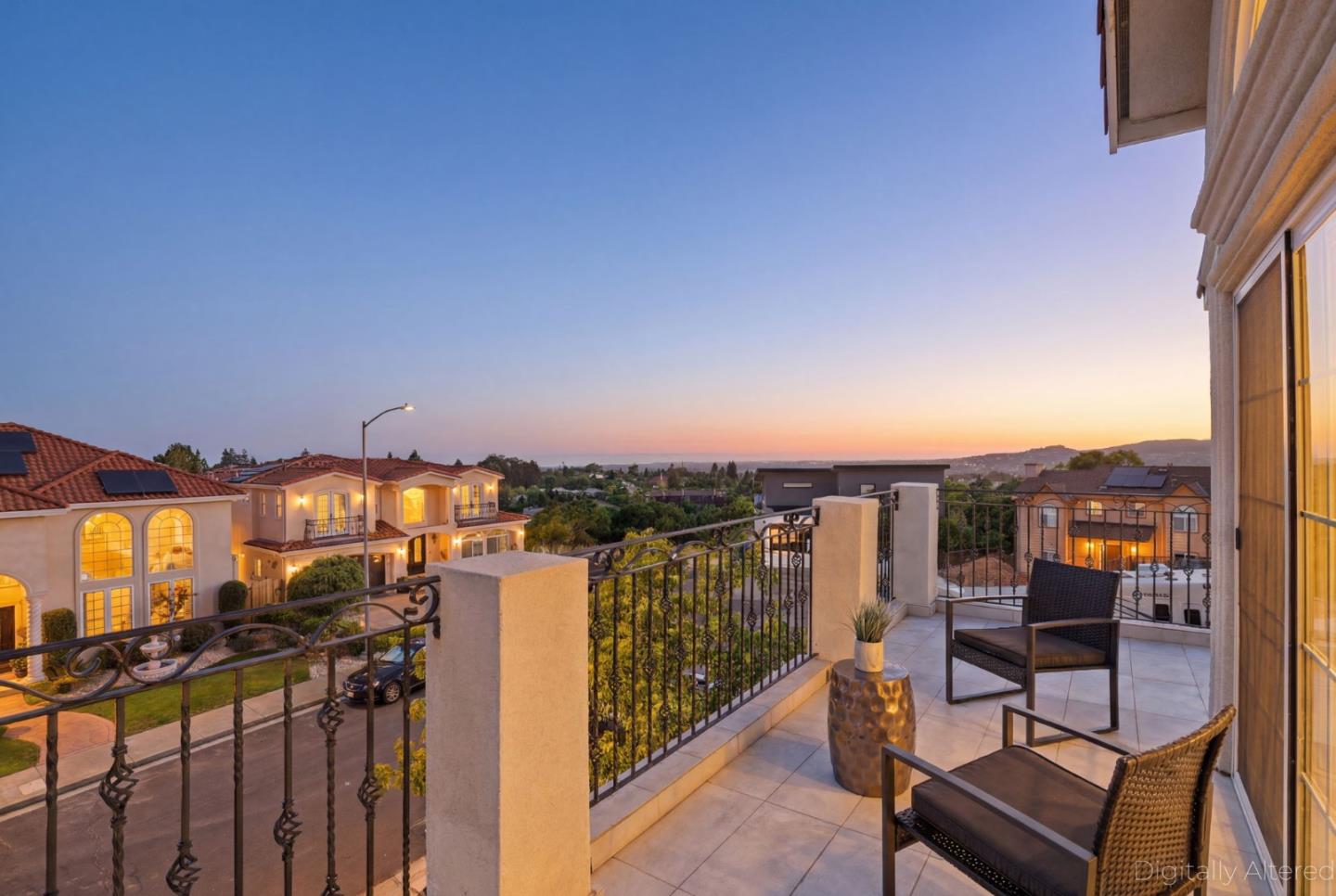 Furnished balcony overlooks nearby homes and hills beneath a blue-and-orange sunset sky.