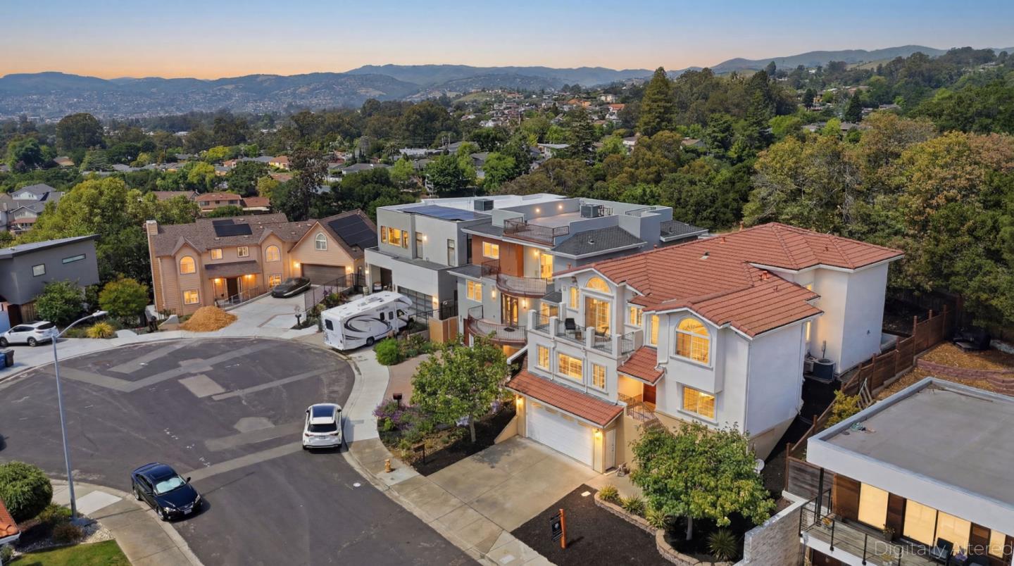 Large white multi-level home with red tile roofs, viewed from above at sunset.
