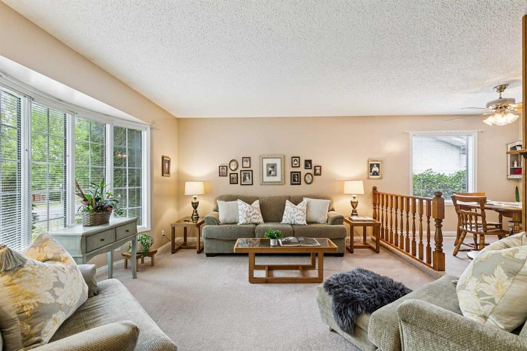Living room with a gray sofa, wide windows, and a dining area beyond the railing.