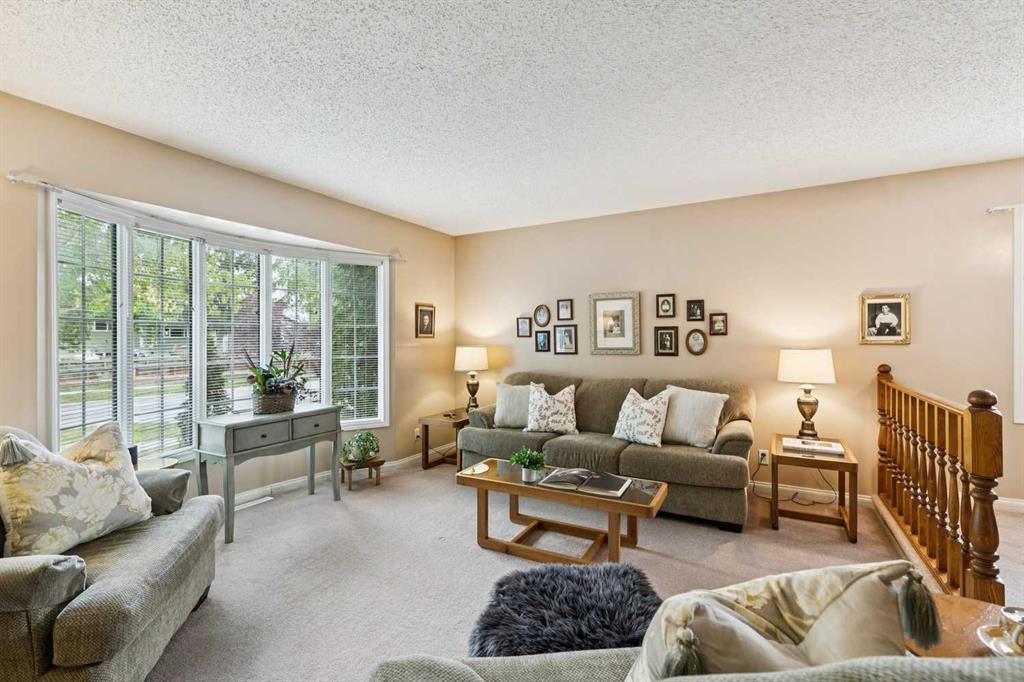 Furnished living room with large windows, a central sofa, and a wooden stair railing.