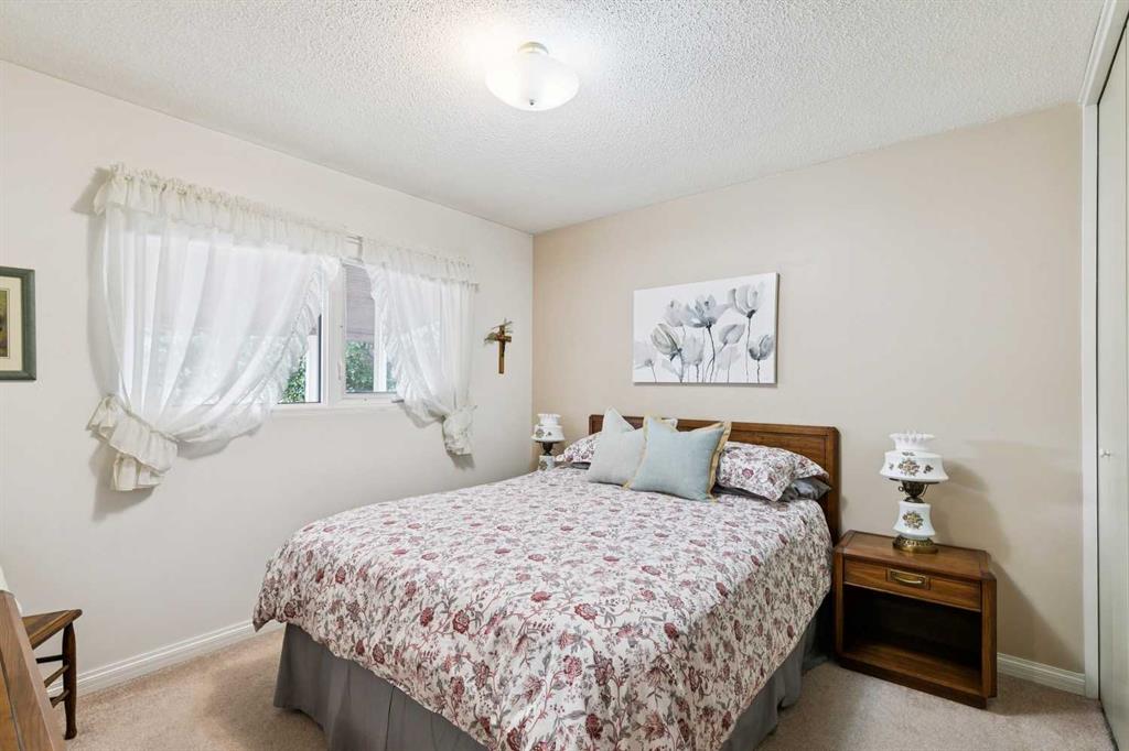 Bedroom with a floral bedspread, wooden nightstand, and curtained window.