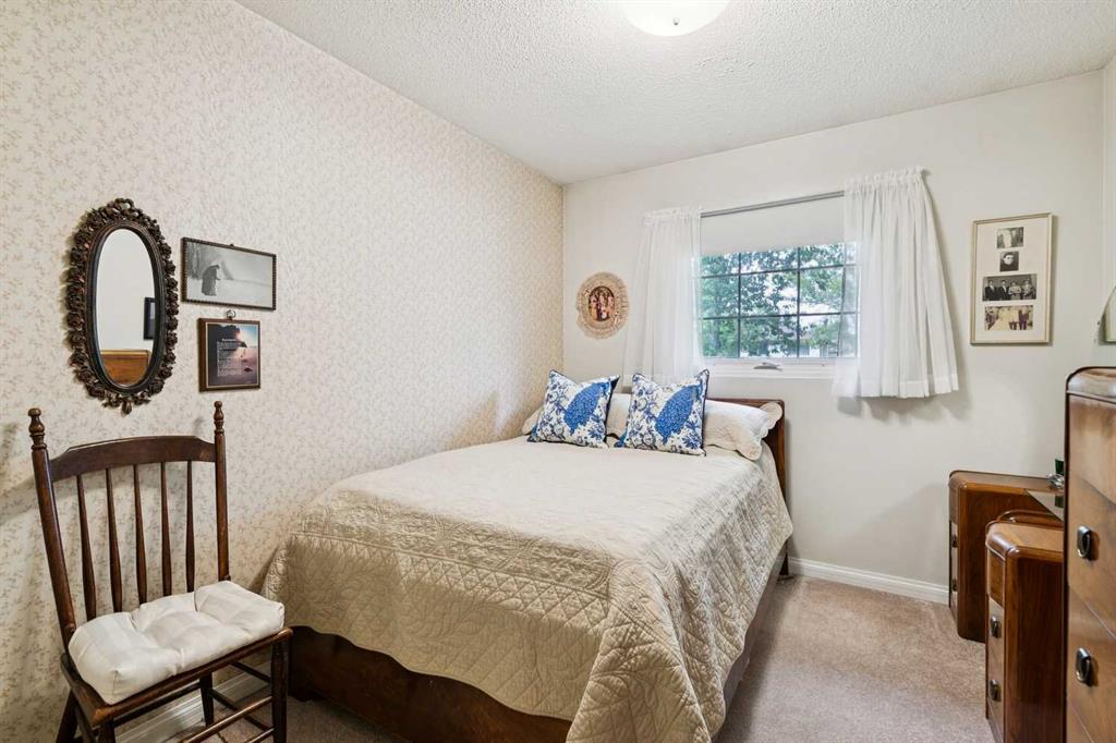 Bedroom with a quilted bed, blue patterned pillows, floral wallpaper, and curtained window.