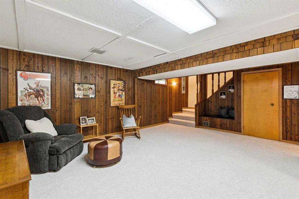 Finished basement sitting area with wood-paneled walls, carpet, and a staircase.