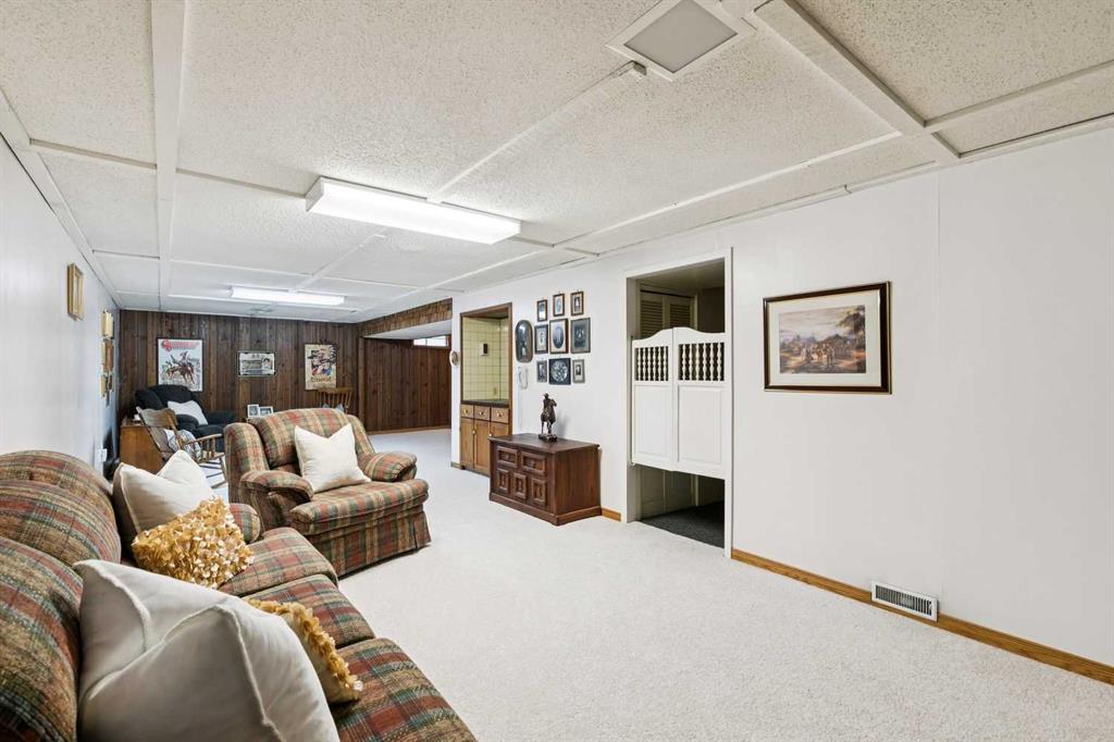 Furnished living room with plaid sofas, wood-paneled walls, and a broad carpeted floor.