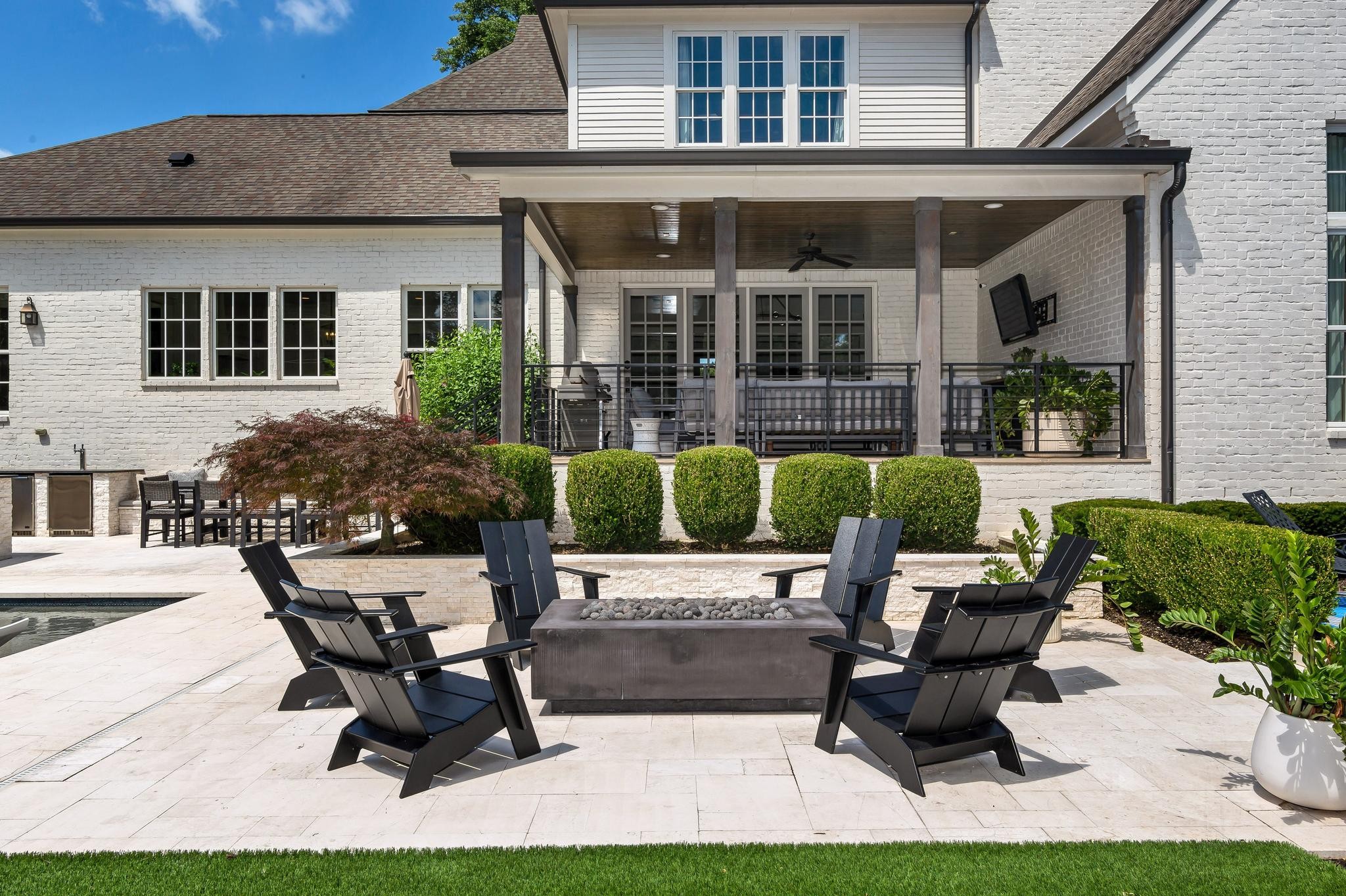 Back patio with covered porch, fire table, lounge chairs, and a glimpse of the pool.