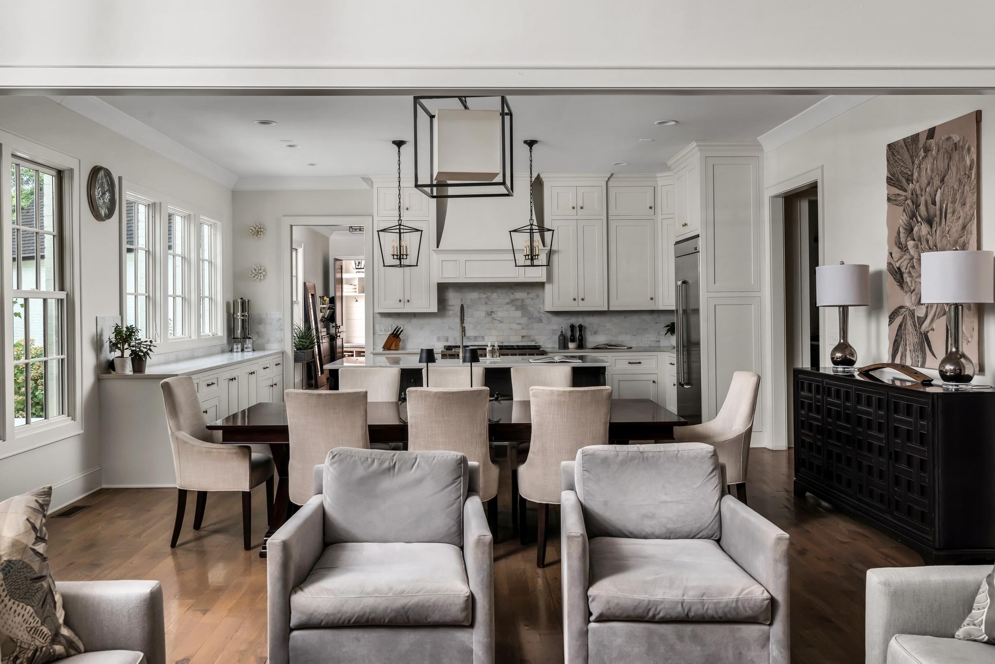 Open-plan kitchen and dining room with white cabinets, marble backsplash, dark table, and upholstered seating.