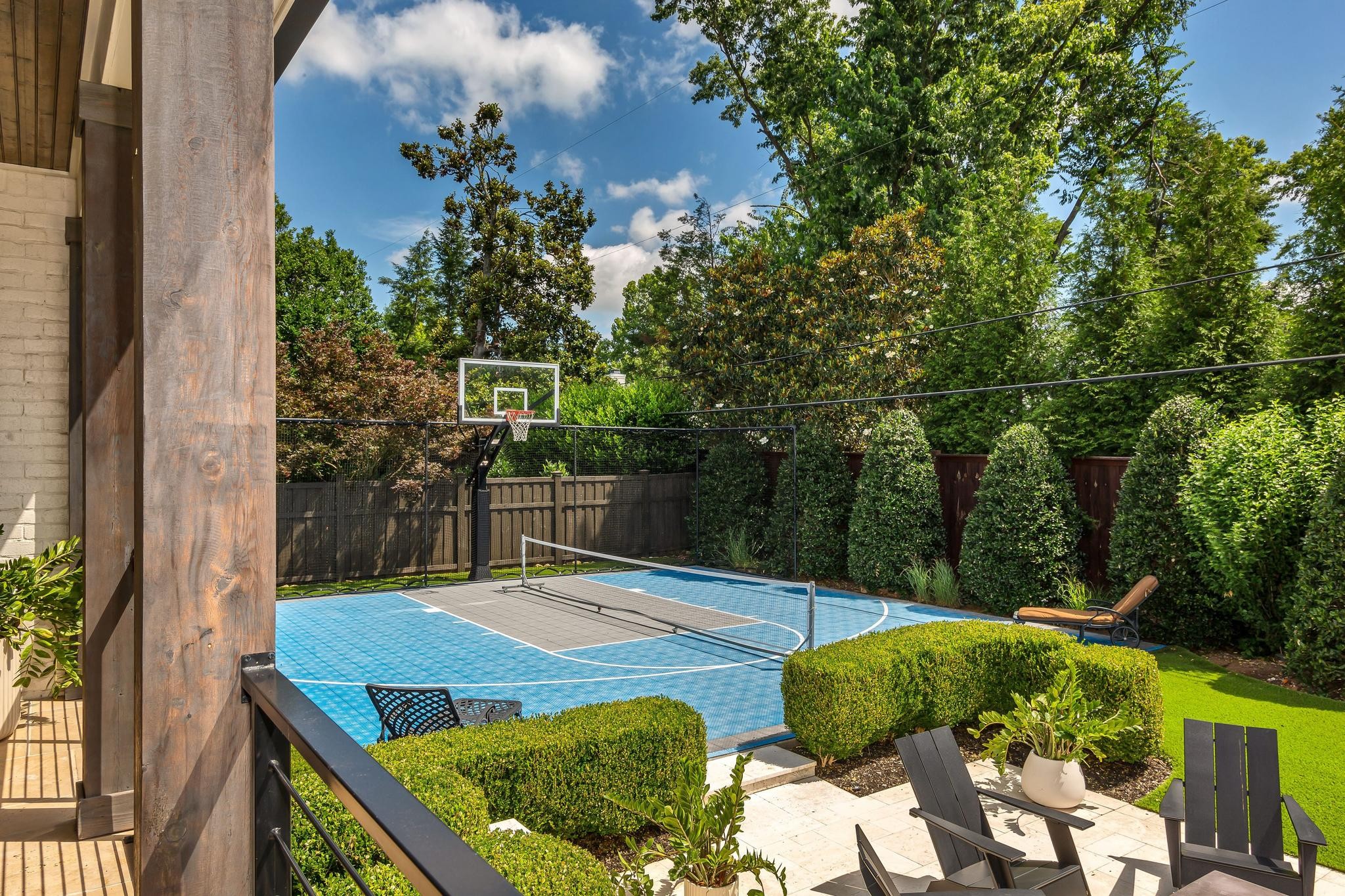 Backyard sports court with a basketball hoop, net, and patio seating