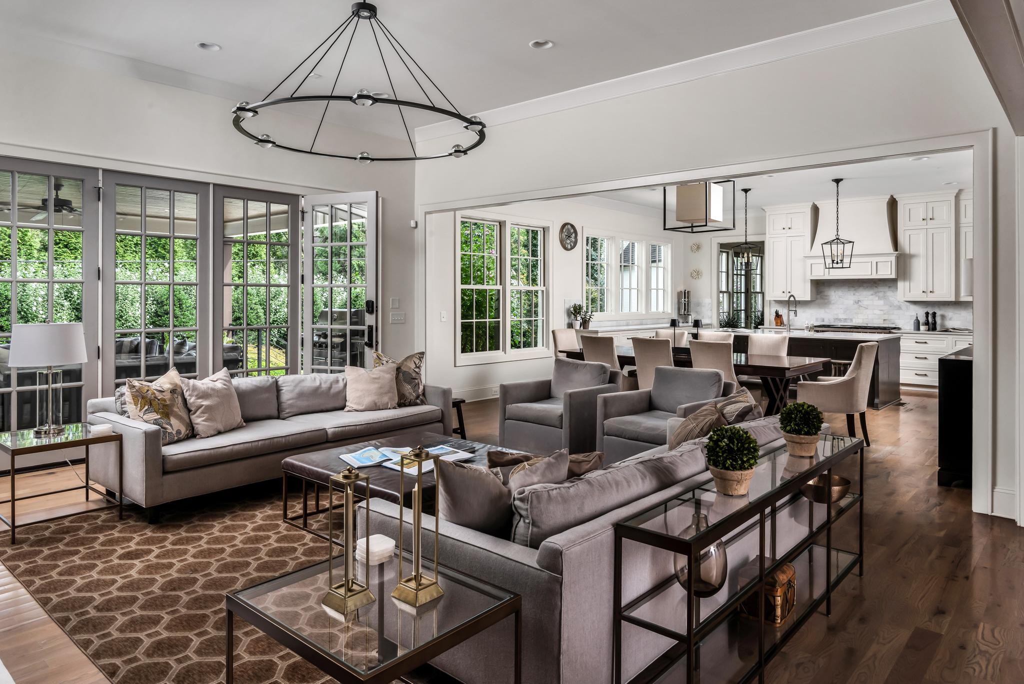 Open-plan living room with gray sofas, large windows, and a dining area beside the kitchen.