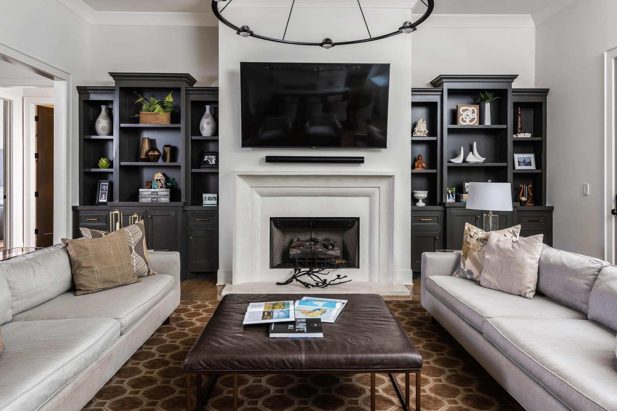 Living room with a white fireplace, television, dark built-ins, and facing light gray sofas.
