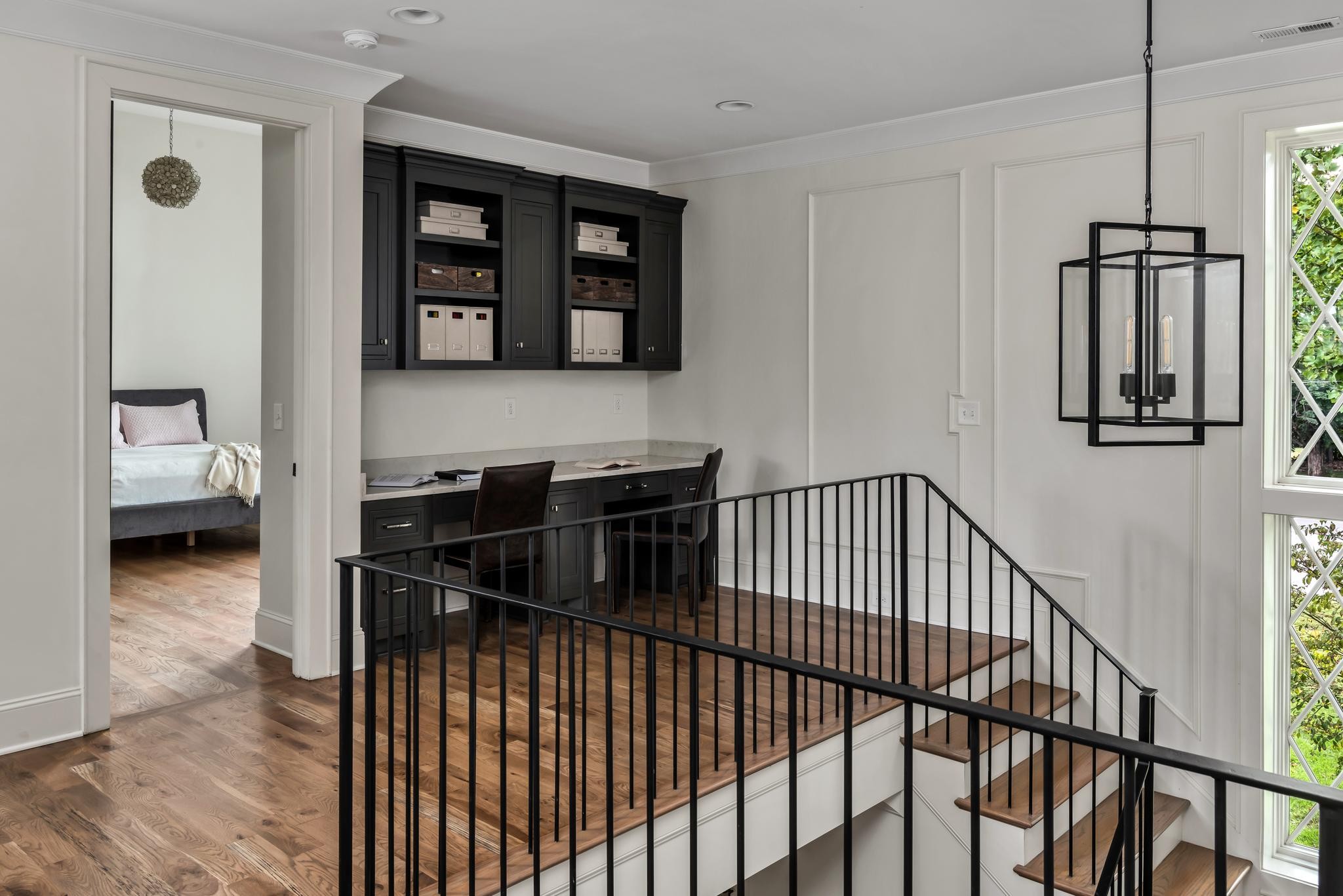 Upstairs landing with built-in desk and shelving beside a hardwood staircase and tall windows.