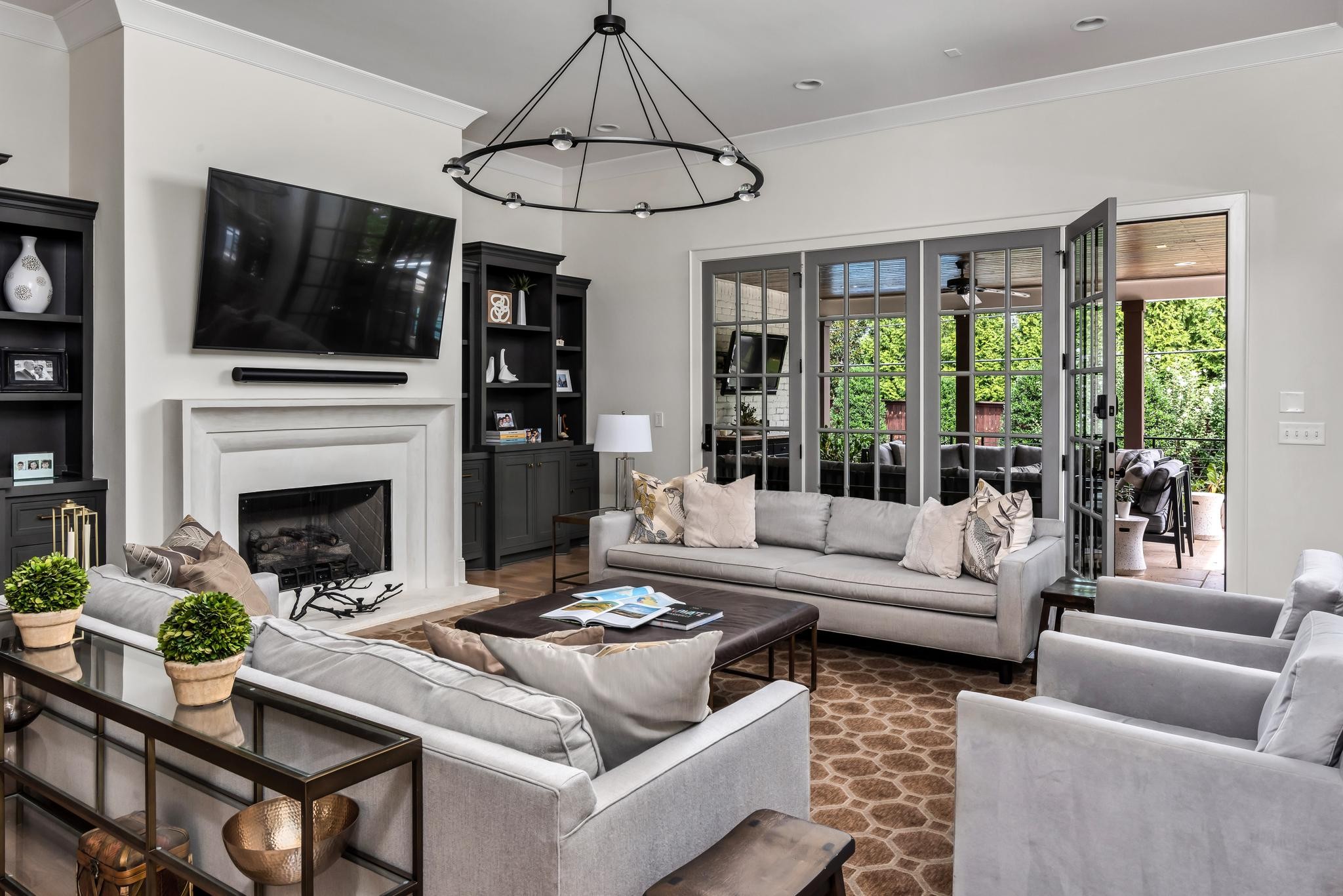 Living room with a white fireplace, gray sofas, and French doors opening to a leafy patio.