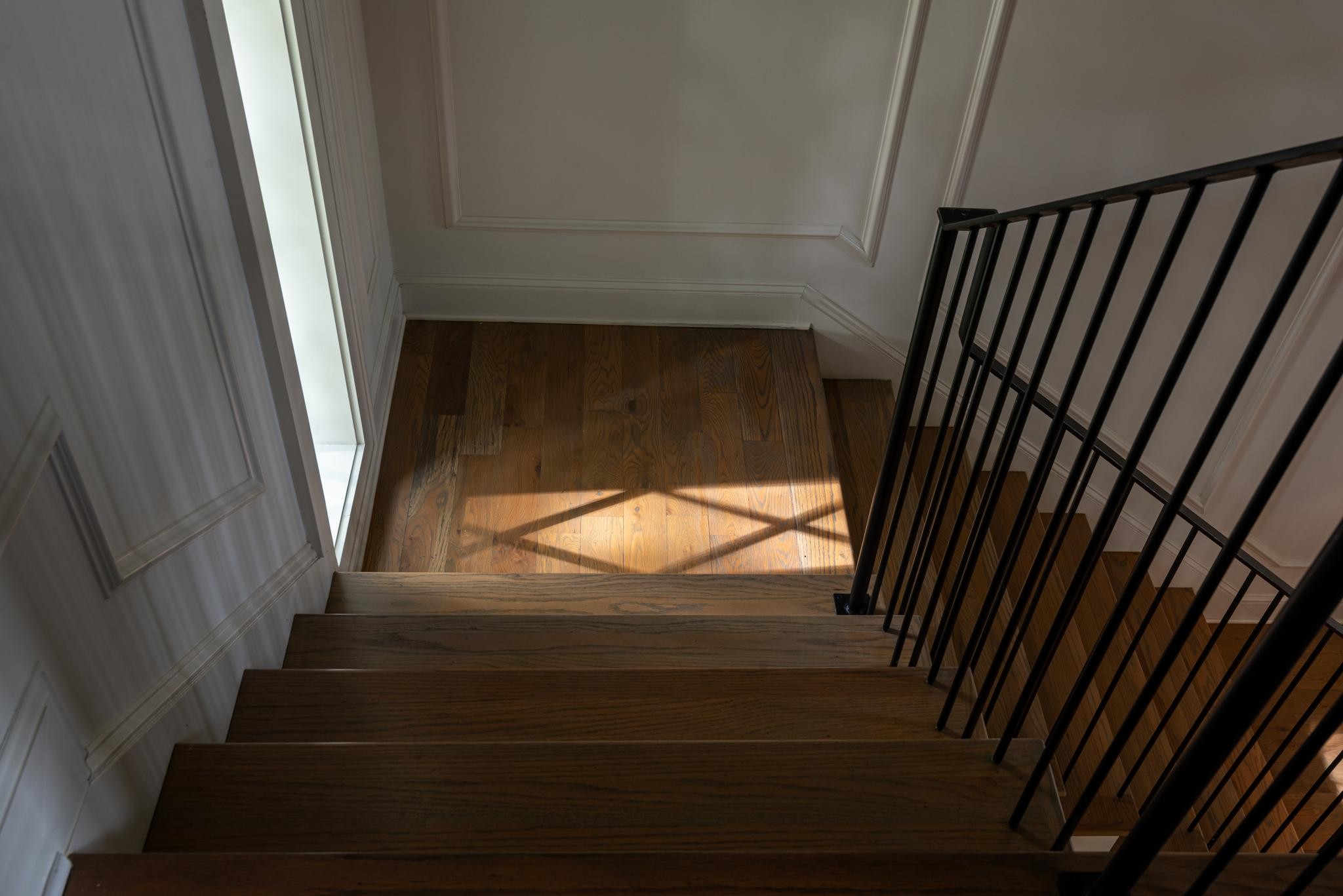 Hardwood staircase with a black metal railing and sunlight crossing the landing.