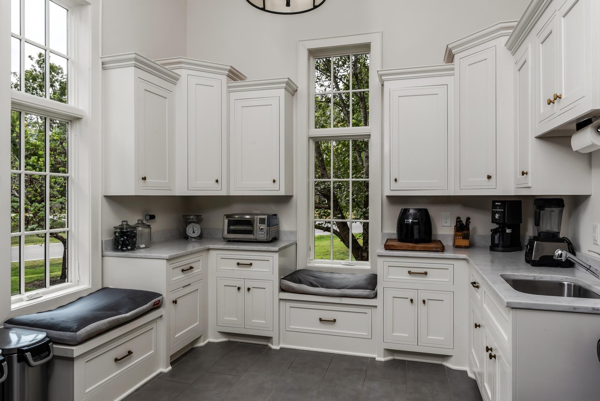 Kitchen with white cabinetry, tall windows, and built-in cushioned window seats.