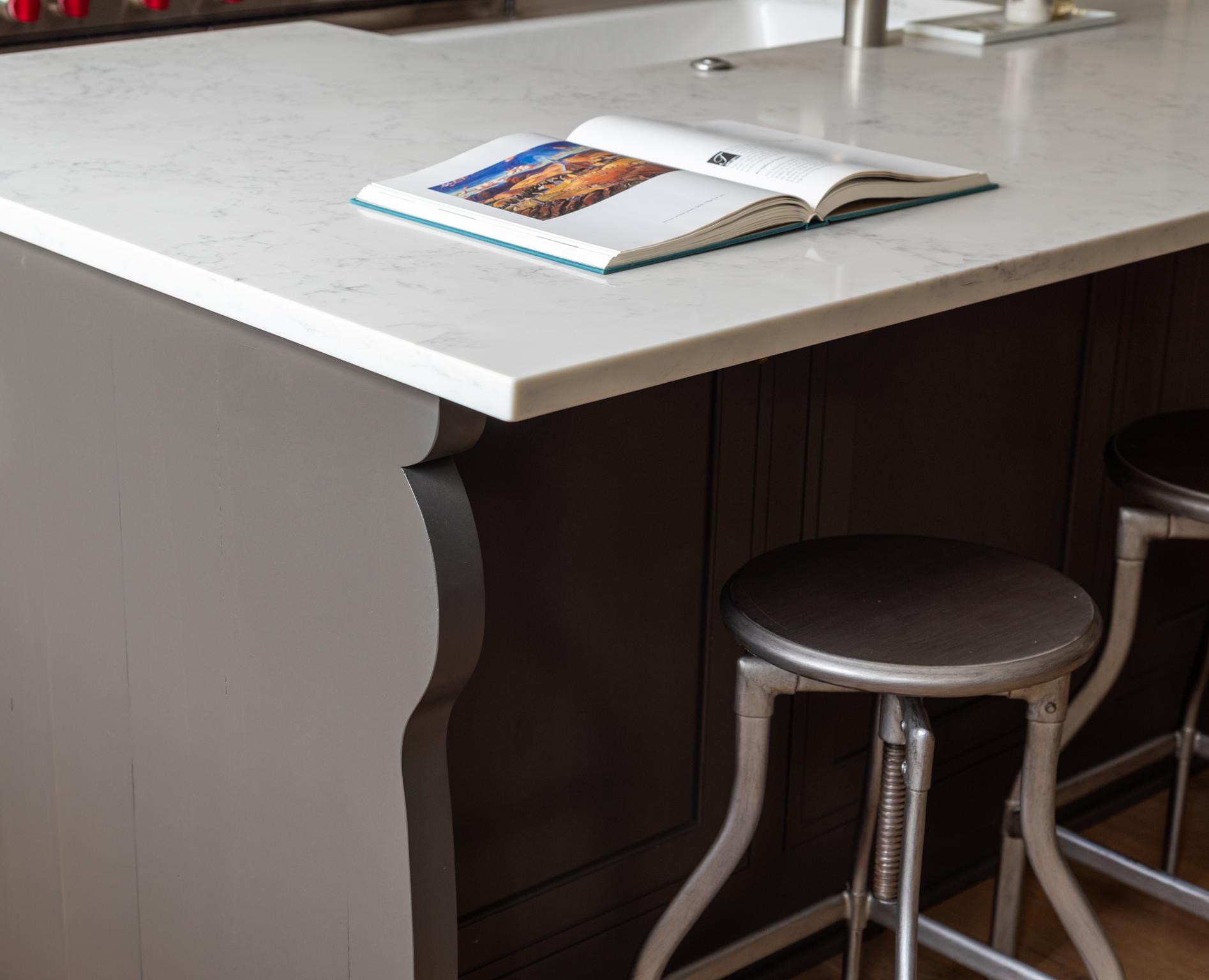 Kitchen island with a white veined stone countertop, dark paneled cabinetry, and metal stools.