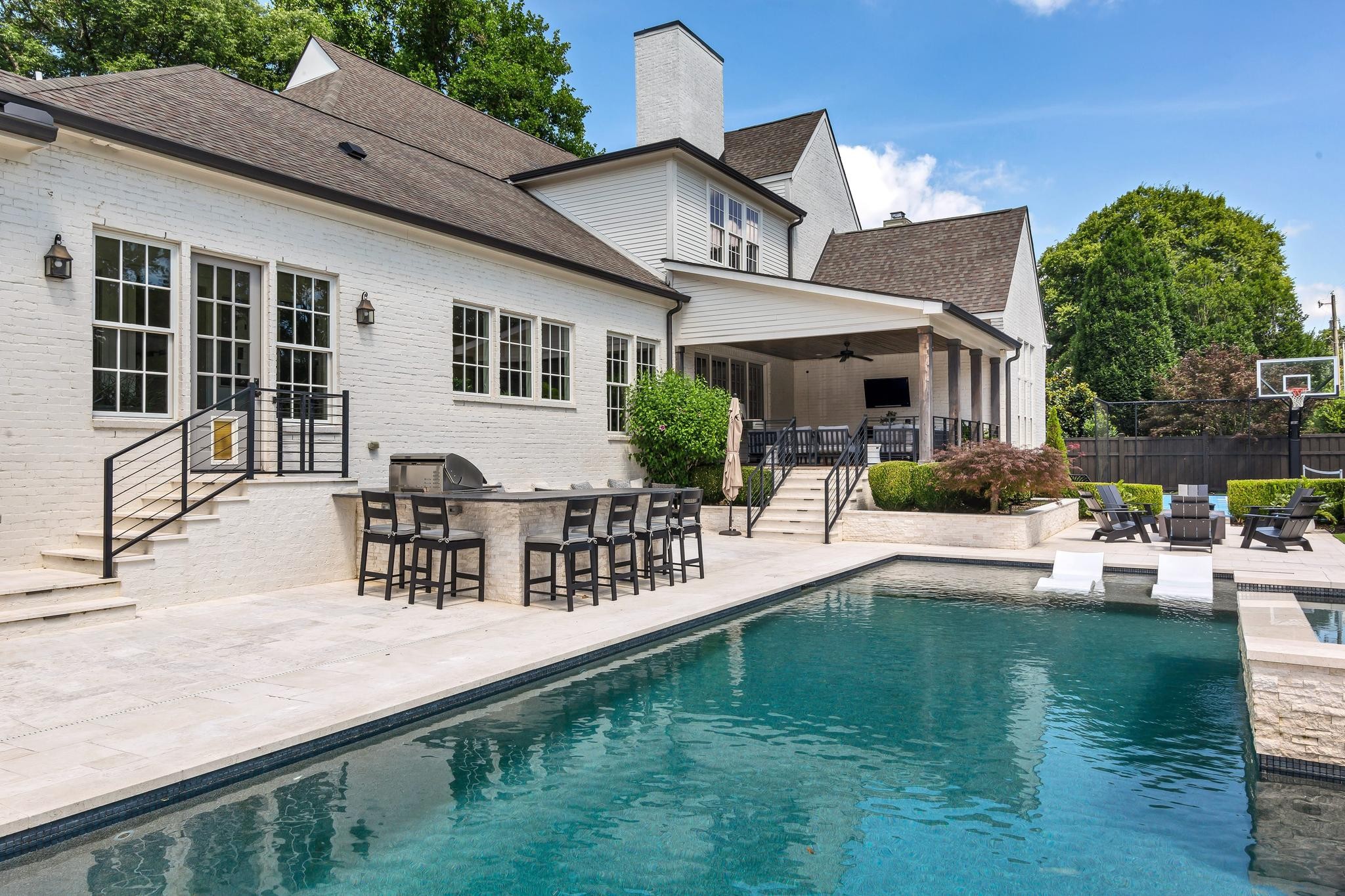 White brick home with covered patio, outdoor dining area, and swimming pool with in-water loungers.