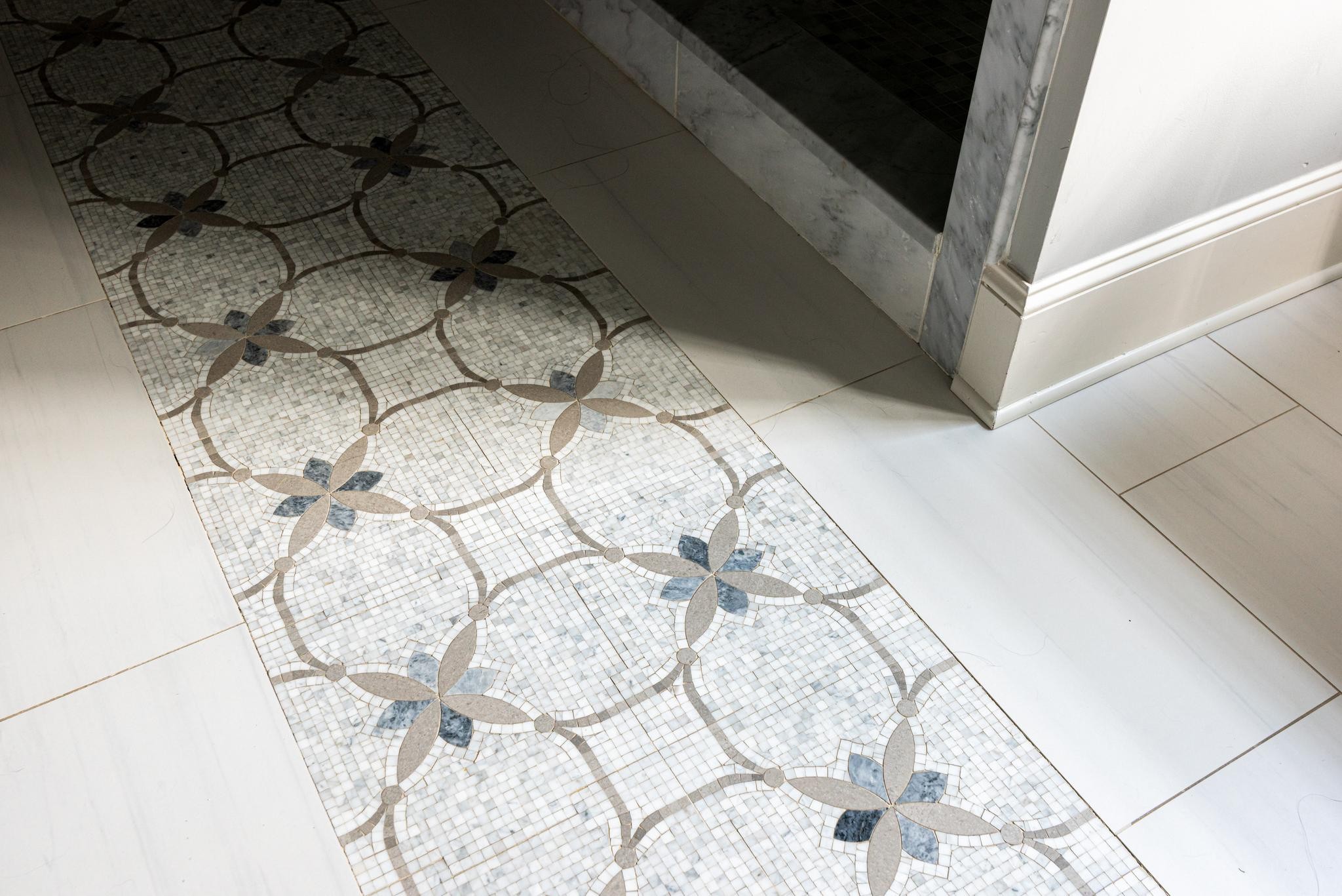 Decorative floral mosaic tile runner bordered by large pale stone floor tiles.