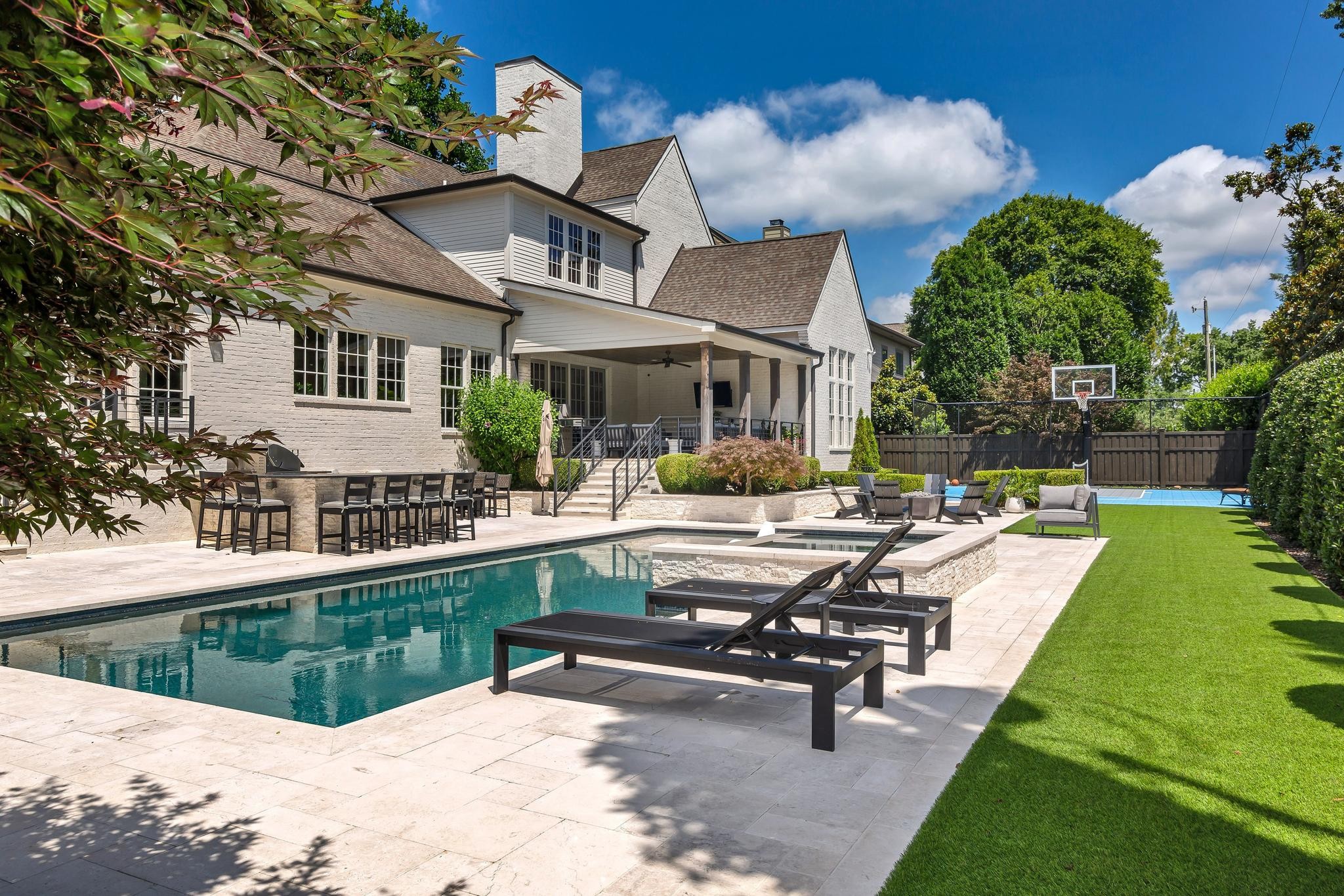 White brick home beside a swimming pool and stone patio, with a covered outdoor dining area and basketball court.