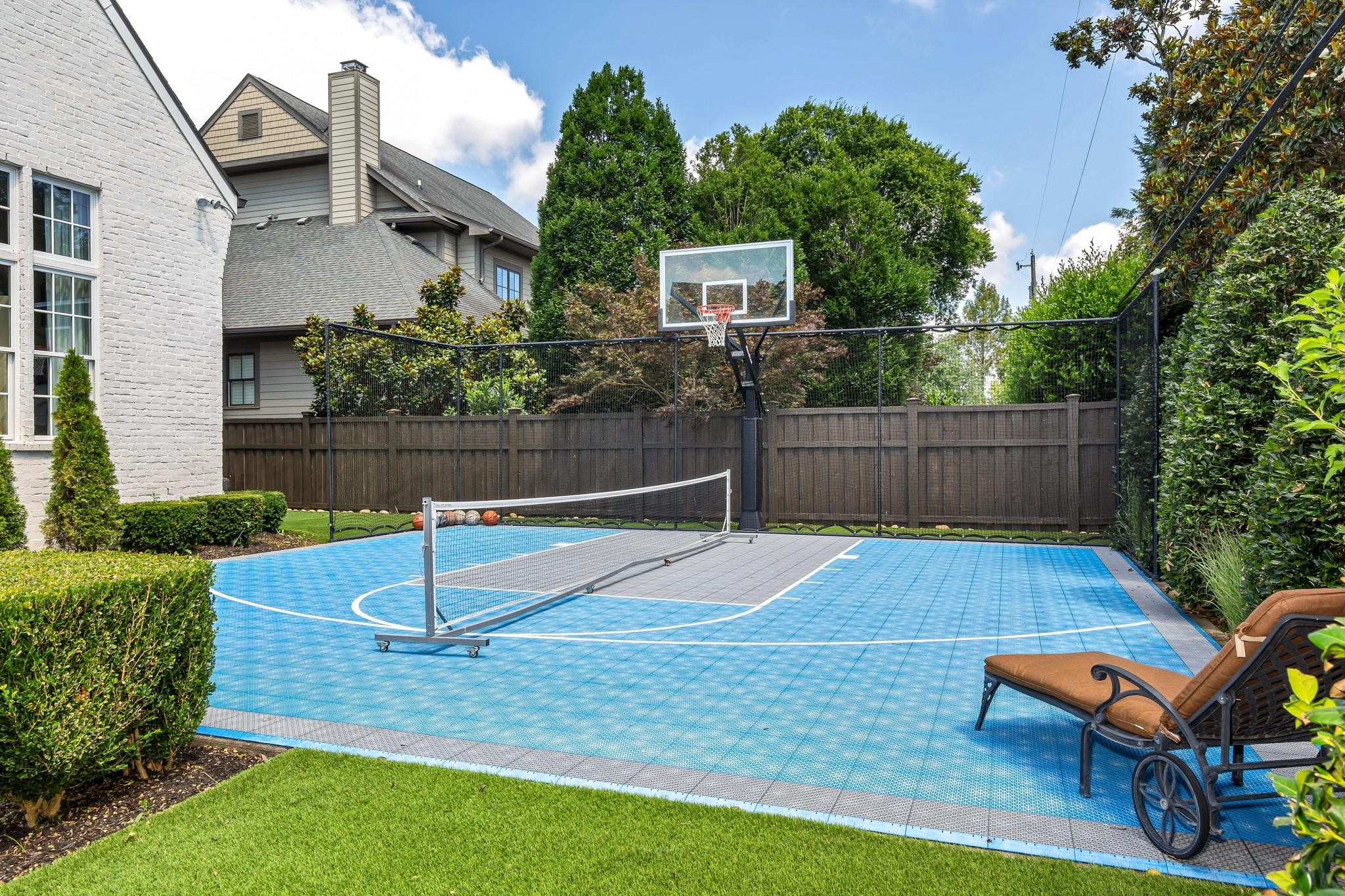 Blue backyard sport court with a net, basketball hoop, and lounge chair